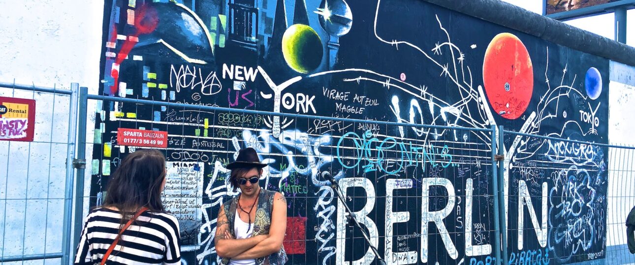 man wearing black waistcoat and white tank tops standing near a mural