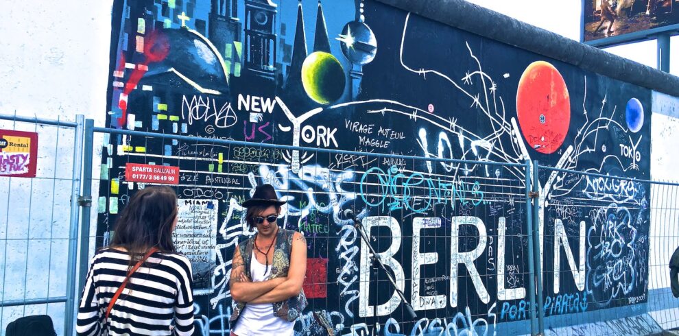 man wearing black waistcoat and white tank tops standing near a mural